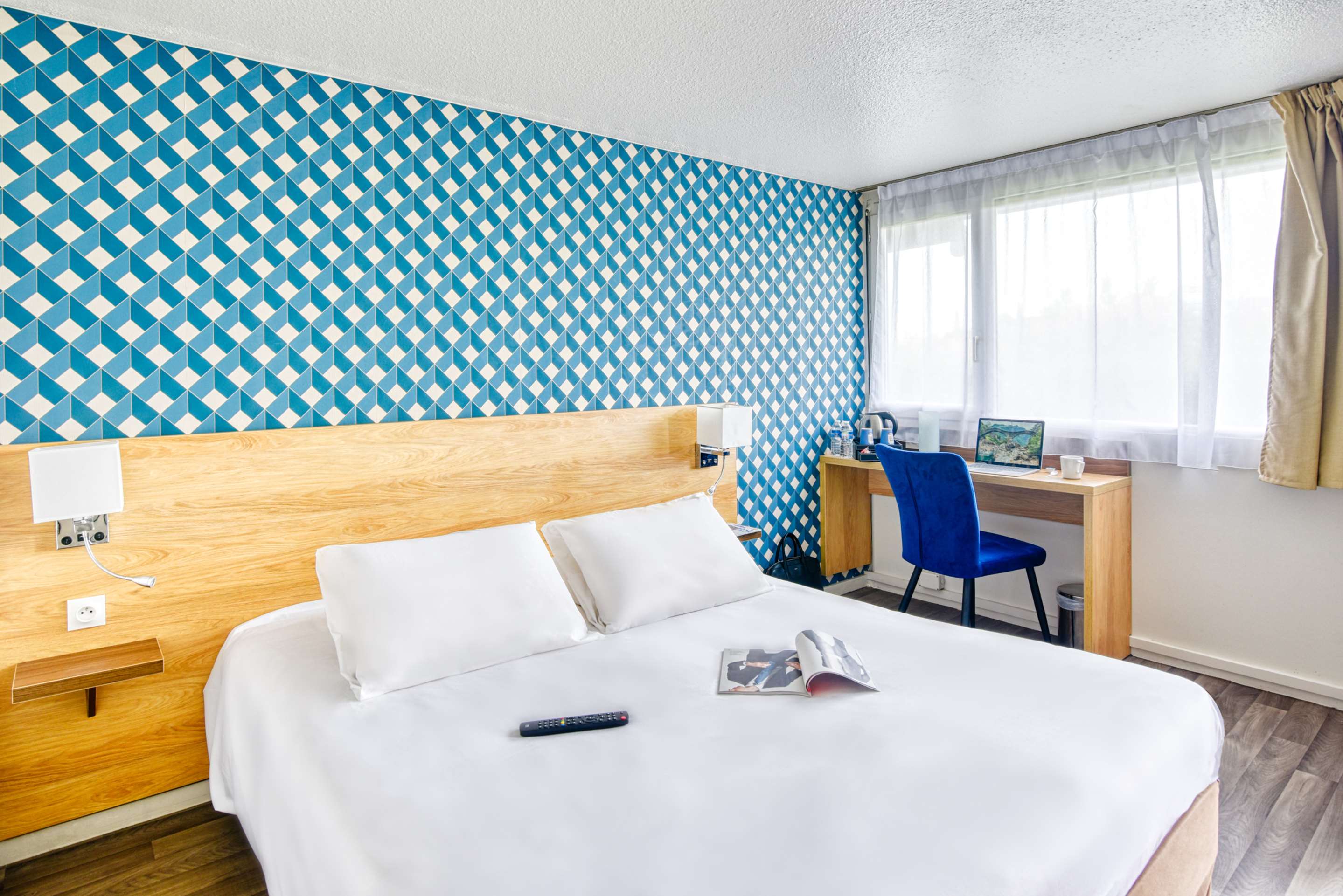 Chambre double avec grand lit, tête de lit en bois, papier peint graphique bleu et bureau