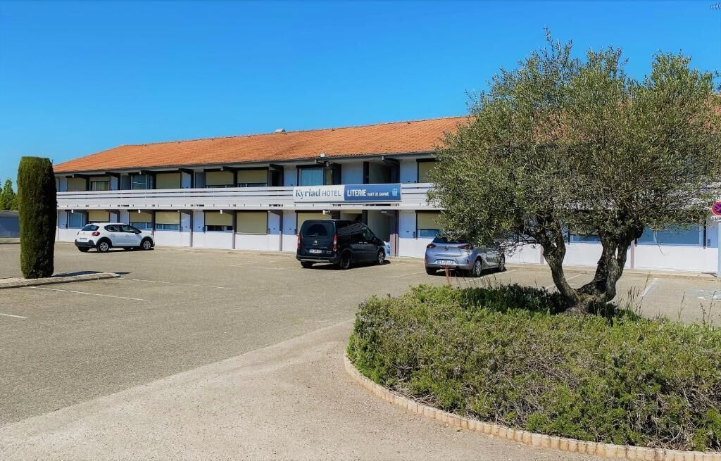 Bâtiment des chambres sur deux niveaux vu depuis le parking, avec un olivier