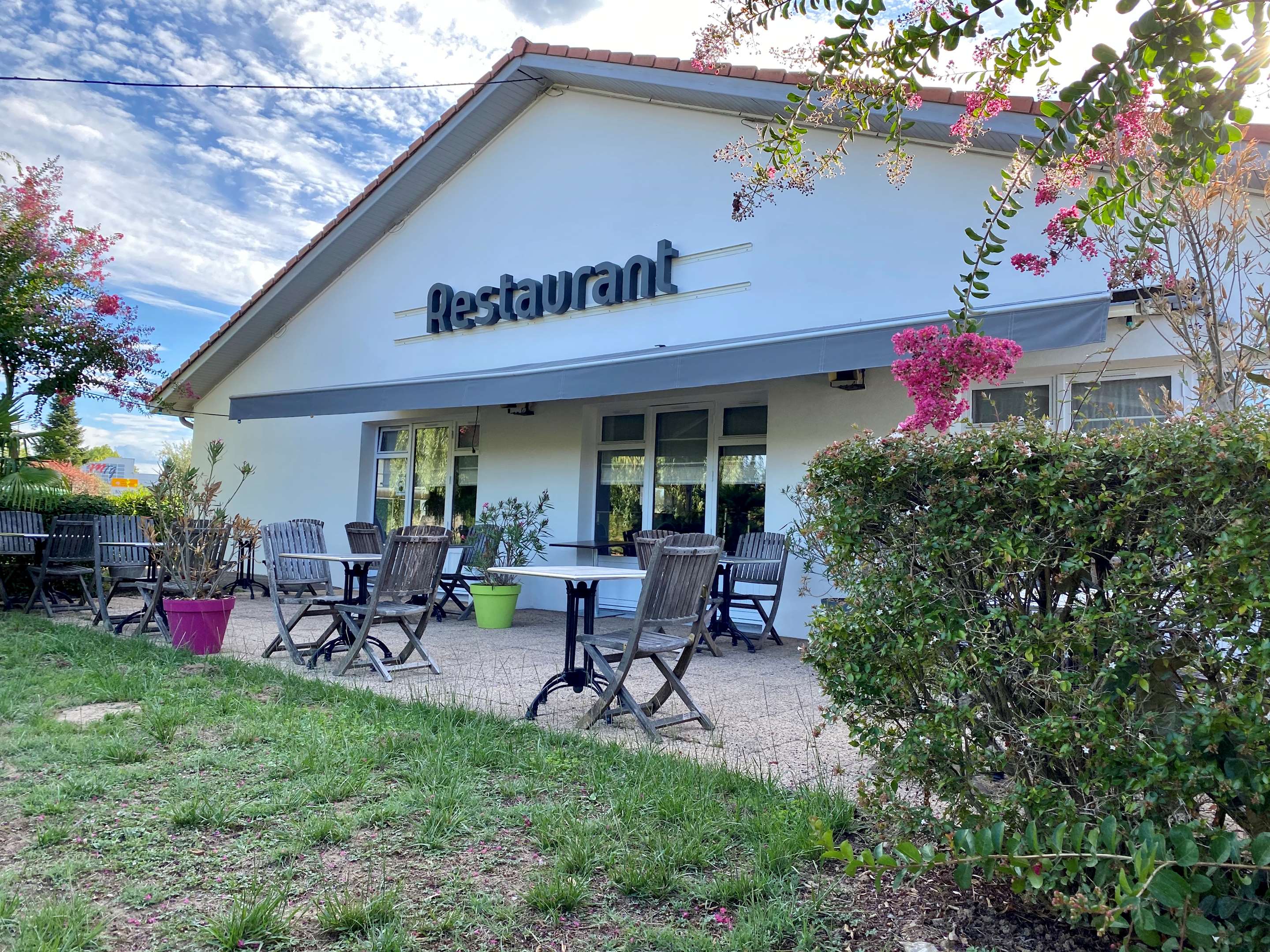 Terrasse du restaurant avec tables et chaises en bois sous un store, fleurs roses au premier plan